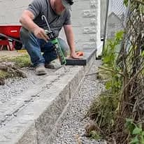 Man applying sealant to a gravel border, ensuring proper landscaping around home.
