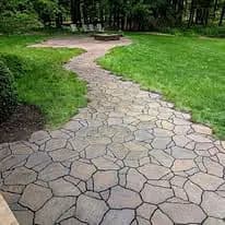 Stone pathway leading to a fire pit in a green backyard setting.
