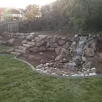 Backyard landscape featuring a natural stone waterfall and lush green lawn.