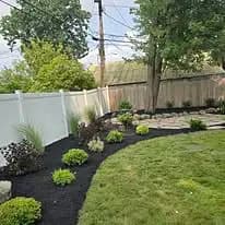 Landscaped garden with plants, mulch, and white fence under a clear sky and power lines.