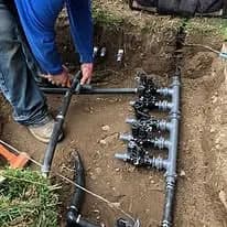 Person installing PVC pipes and valves in a trench for irrigation system.